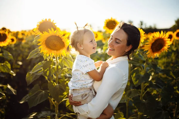 Genç anne ve küçük kızı güneşli bir yaz gününde ayçiçeği tarlasında eğleniyor ve eğleniyorlar. Aileyle yaz tatili. Mutluluk, özgürlük ve aile değerleri kavramı