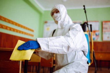 Dezenfeksiyon grubundan bir adam okuldaki masayı sarı bir bezle temizliyor. Profesyonel işçi, covid-19 'un yayılmasını önlemek için sınıfı sterilize ediyor. Öğrencilerin ve öğrencilerin sağlık hizmetleri kavramı