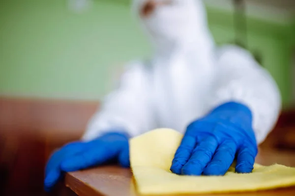Closeup of a man from disinfection group cleans up the desk at school with a yellow rag. Professional worker sterilizes the classroom to prevent covid-19 spread. Healthcare of pupils and students