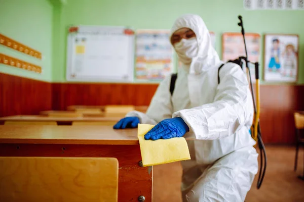 A man from disinfection group cleans up the desk at school with a yellow rag. Professional worker sterilizes the classroom to prevent covid-19 spread. Healthcare of pupils and students concept