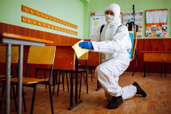 A man from disinfection group cleans up the desk at school with a yellow rag. Professional worker sterilizes the classroom to prevent covid-19 spread. Healthcare of pupils and students concept
