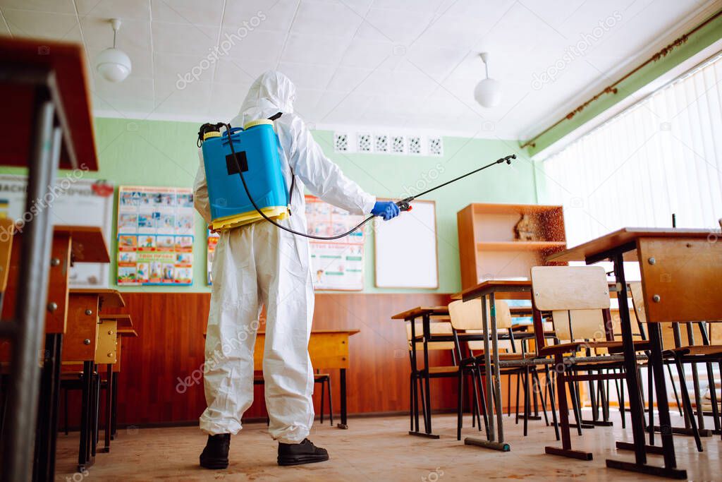 A man wearing a sanitizing equipment and protective suit disinfects the classroom to prevent coronavirus spread among students and pupils. Health care and covid-19 prevention concept