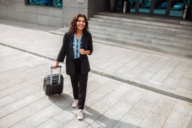 Genç iş kadını otelin yakınında resmi takım elbise giymiş bir bavulla yürüyor. İş gezisindeki bir kadın otelden çıkış yapıyor ve taksi bekliyor. İş ve seyahat kavramı