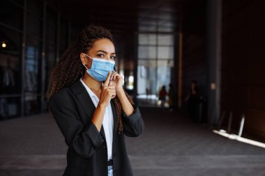 Tıbbi maske takan genç bir iş kadını cep telefonuyla konuşurken parmağının ağzının yanında sessizlik işareti gösteriyor. Covid-19 salgını sırasında bilgi eksikliği