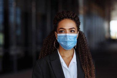 Ofis binasının dışında steril tıbbi maske takan genç bir iş kadınının portresi. Coronavirus dünya çapında karantina sırasında önleme yayıldı. Önde gelen iş dünyası Covid-19
