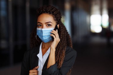 Ofis binasının dışında steril maske takarak iş konuşan genç ve çekici bir kadının portresi. Covid-19 salgınında önde gelen şirketler