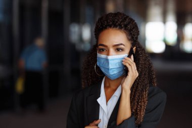 Ofis binasının dışında steril maske takarak iş konuşan genç ve çekici bir kadının portresi. Covid-19 salgınında önde gelen şirketler