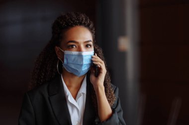 Ofis binasının dışında steril maske takarak iş konuşan genç ve çekici bir kadının portresi. Covid-19 salgınında önde gelen şirketler