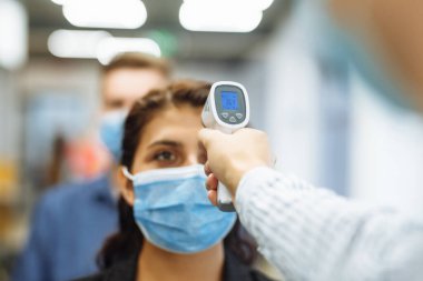 Ofis çalışanları koronavirüs salgını sırasında uzak temas olmayan bir termometreyle kontrol edilir. Ofis koridorunda sıcaklık kontrolünü geçen genç bir iş kadını covid-19 yayılmasını önlemek için.