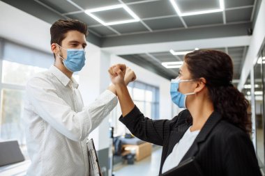 Koronavirüsün yayılmasını önlemek için genç işçilerin Coronavirus sırasında özel selamı. Tıbbi maskeli bir adam ve kadın ofiste birbirlerini selamlamak için ellerini çaprazladılar. İş yerinde sağlık güvenliği