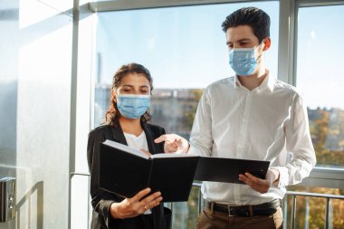 İki meslektaş, küresel salgın sırasında koronavirüs hastalığından korunmak için sağlık maskesi takarak ofis koridorunda iş konularını tartışıyor. Çalışma konseptinde sağlık güvenliği