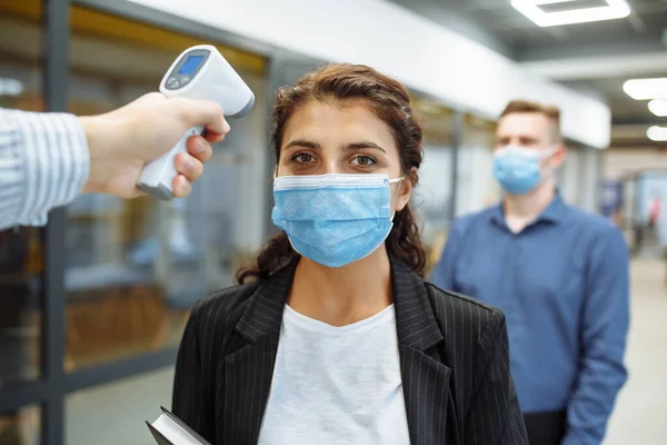 Office workers are checked with a distant non contact thermometer during coronavirus pandemic. Young business woman passing temperature control at the office corridor to prevent covid-19 spread