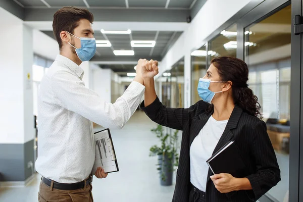 Young workers\' special greeting during coronavirus to prevent coronavirus spread. Man and woman wearing medical masks crossed their hands to greet each other at the office. Health safety at work