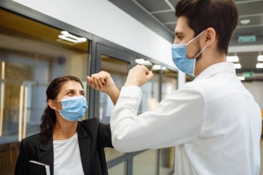 Koronavirüsün yayılmasını önlemek için genç işçilerin Coronavirus sırasında özel selamı. Tıbbi maskeli bir adam ve kadın ofiste birbirlerini selamlamak için ellerini çaprazladılar. İş yerinde sağlık güvenliği