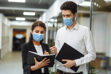 İki meslektaş iş ve iş hakkında konuşuyor. Ofisin koridorunda koruyucu steril tıbbi maskeler takıyorlar. Koronavirüs küresel pandemik konsept sırasında önleme yayıldı