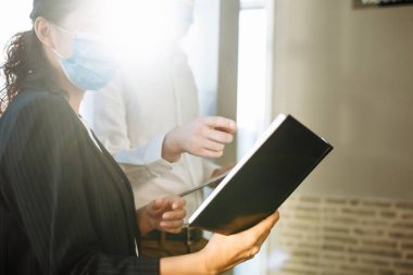 İki meslektaş, küresel salgın sırasında koronavirüs hastalığından korunmak için sağlık maskesi takarak ofis koridorunda iş konularını tartışıyor. Çalışma konseptinde sağlık güvenliği