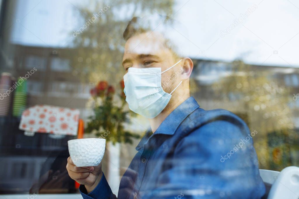 Portrait of a man working from a cafe on a laptop remotely. Businessman leading matters in a distance with a cup of coffee during coronavirus pandemic quarantine. Health care and safety concept