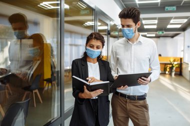 İş adamları koronavirüs salgını sırasında çalışma sorunlarını tartışıyor. Korumacı tıbbi maskeler takan kadın ve erkek ofis koridorunda iş konuşuyorlar. Çalışma konseptinde sağlık güvenliği