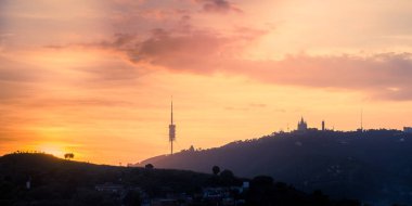 Barselona'da kilise ve iletişim kulesi ile Tibidabo dağına bakan gün batımı. Catalonia, İspanya