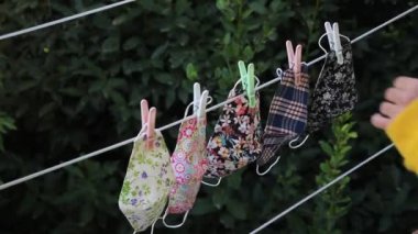 Dışardaki saç kurutma makinesinden tekrar kullanılabilir yüz maskeleri toplayan ve çamaşır ipiyle naylon bir ipe asılan biri. Maskelerin yeniden kullanılması kavramı.