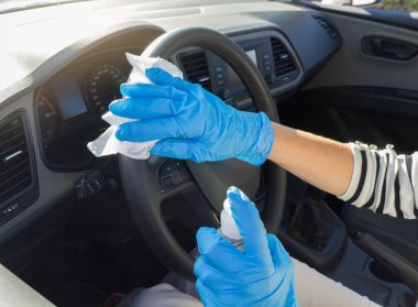 Kısmen mavi lateks eldivenli kadın Coronavirus salgını sırasında arabanın içini dezenfekte etmek için antiseptik ve bez kullanıyor. Yüz maskeli yaşlı İspanyol kadın arabasını kullanıyor..