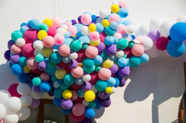 Beyaz duvarda kalp şeklinde bir sürü renkli balon var..