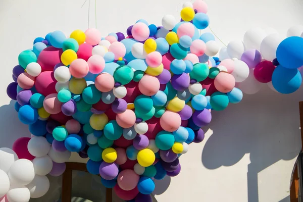 Many colorful balloons in the form of a heart on a white wall background.