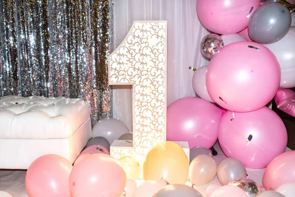 Neşeli bir sahne, büyük, parıldayan bir numaralı süslemeyle ilk doğum gününü kutlar. Arkaplanda pırıl pırıl gümüş perdeler var, festival atmosferini güçlendiriyor.