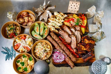 A variety of dishes is arranged beautifully on a wooden platter for a holiday feast. Grilled meats, fresh salads, and colorful sides are served in stylish bowls, making it a perfect setting for a festive gathering with friends and family.