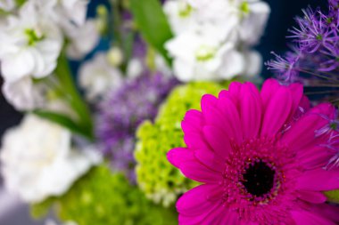 A vibrant bouquet features pink gerbera daisies, white blooms, green accents, and purple flowers. This lively arrangement showcases a beautiful mix of colors, perfect for brightening any space and celebrating nature's charm.