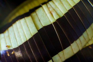 Thin slices of eggplant are neatly arranged, showcasing its light and dark purple colors. The texture and symmetry of the slices highlight the vegetable's freshness, perfect for a healthy dish or side.