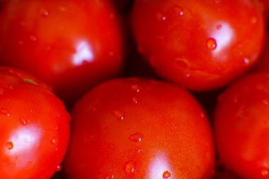Bright red tomatoes sit closely together on a wooden table, glistening with water droplets. The vibrant color and smooth texture highlight their freshness, making them look delicious and ready to be used in a meal or salad.