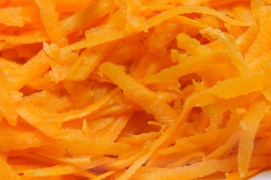 Bright orange, finely grated carrots are gathered together on a surface. The texture is vibrant and fresh, indicating they are perfect for salads, garnishes, or cooking. The scene conveys a sense of healthy food preparation.