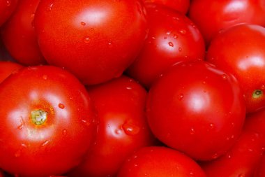 Bright red tomatoes are piled together, glistening with water droplets, showcasing their freshness. This vibrant display highlights the natural beauty of the produce, perfect for summer meals or recipes.