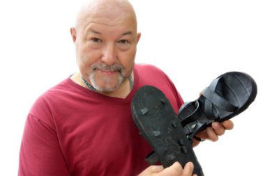 Acımasız, sakallı, gülümseyen bir adam ellerinde lastik terlikler tutuyor.