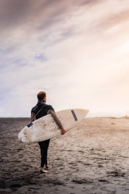 Gün batımında denize yürüyen sörfçü adam.