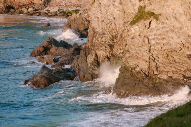 Deniz dalgaları kayalıklara, doğal plaja ve sudaki kayalara karşı kırılıyor