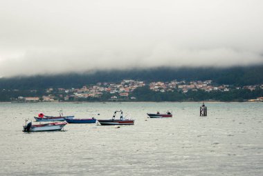 Bir deniz köyü teknelerle bir nehrin arkasında görülüyor.