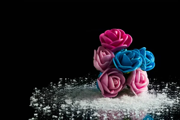 Colorful artificial flowers on crushed ice on a black background isolate