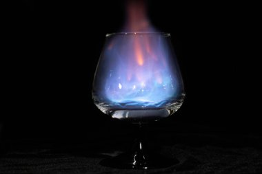 Yalnız siyah bir arka plan üzerinde yanan bir sambuca ile Konyak cam