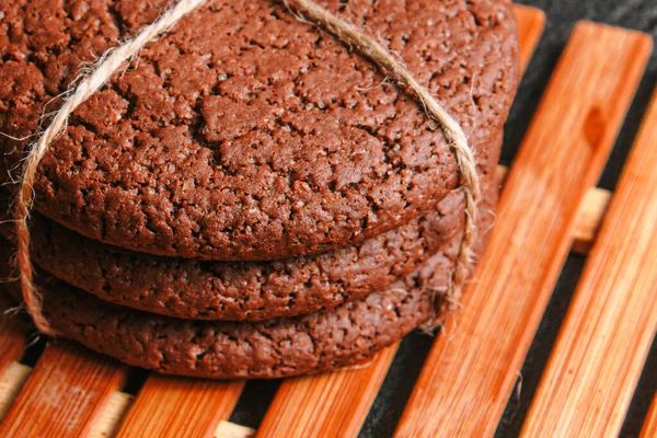 Biscoitos de aveia de chocolate amarrados com uma corda estão em uma placa de bambu em concreto preto. de perto — Fotografia de Stock