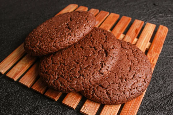 Três biscoitos de aveia de chocolate estão em uma folha de bambu em concreto preto. flat lay vista superior — Fotografia de Stock