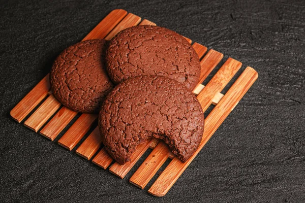 Biscoitos de aveia de chocolate três peças um mordido encontra-se em uma placa de bambu em concreto preto — Fotografia de Stock