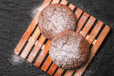 iki çikolatalı yulaflı kurabiye üzerine pudra şekeri serpiştirilmiş siyah betonun üzerindeki bambu tabağında yatıyor. düz üst görünüm