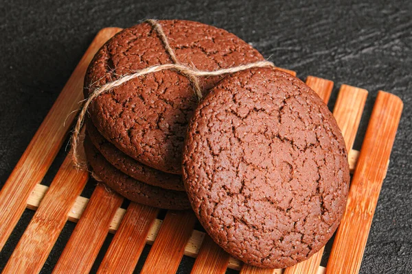 Biscoitos de aveia de chocolate amarrados com uma corda estão em uma placa de bambu em concreto preto — Fotografia de Stock