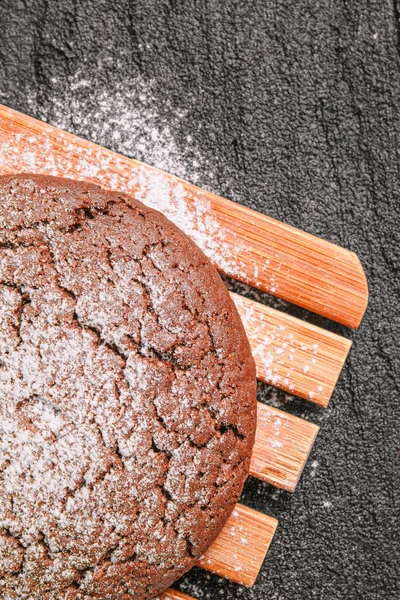 Biscoitos de aveia de chocolate polvilhado com açúcar em pó encontra-se em uma placa de bambu em concreto preto. flat lay vista superior — Fotografia de Stock