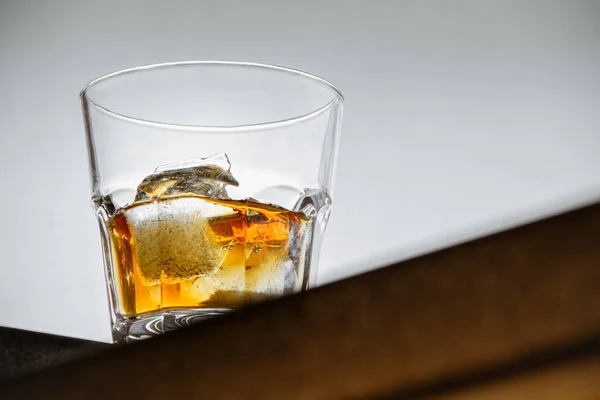 Na rohu pultu na světle šedém pozadí stojí sklenice whisky s ledem. zblízka, pohled bota, kopírovací prostor. horizontální orientace — Stock fotografie