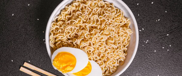 Susam tohumlu bir tabakta erişte bambu çubukları, yakın plan siyah bir masada haşlanmış yumurta. Düz ley. Boşluğu kopyala.