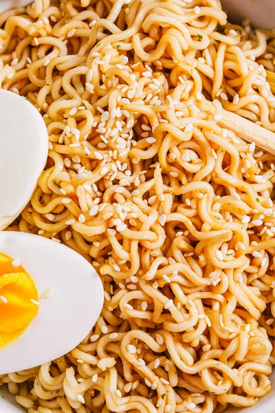 Nudeln in einem Teller mit Sesam und Sojasauce, Bambusstäbchen, gekochte Eier auf einem schwarzen Tisch in Großaufnahme. flach. Kopierraum. — Stockfoto