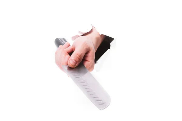 Mano maschile con uno chef con un coltello attraverso un buco di carta su uno sfondo bianco isolato. chiudere, copiare lo spazio. — Foto Stock